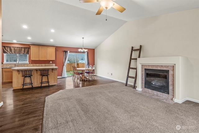 living room featuring ceiling fan with notable chandelier, sink, vaulted ceiling, a fireplace, and dark hardwood / wood-style flooring