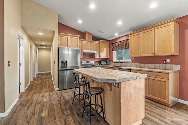 kitchen featuring a center island, stainless steel appliances, hardwood / wood-style floors, vaulted ceiling, and a breakfast bar