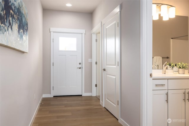 doorway to outside with light wood-style floors, baseboards, a sink, and recessed lighting