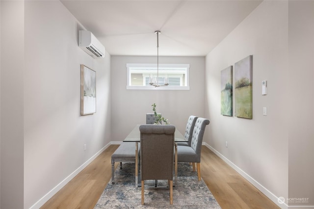 dining area featuring a notable chandelier, light wood finished floors, a wall mounted AC, and baseboards