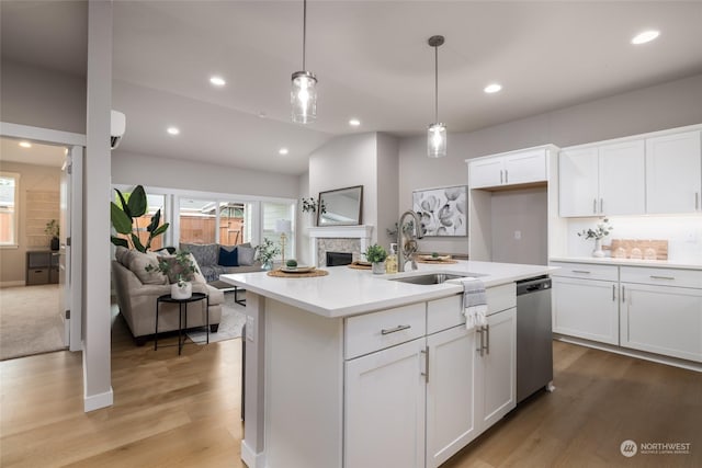 kitchen featuring light wood finished floors, open floor plan, stainless steel dishwasher, white cabinetry, and a sink