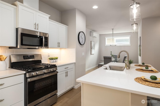 kitchen with light countertops, decorative backsplash, appliances with stainless steel finishes, an AC wall unit, and a sink