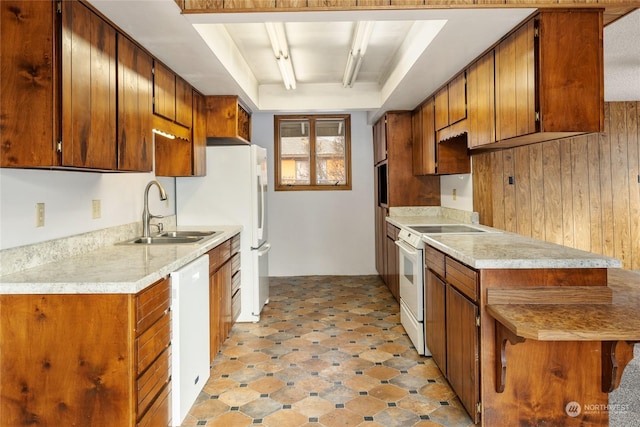 kitchen with a kitchen bar, white appliances, sink, and wooden walls