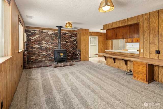 interior space featuring carpet flooring, a wood stove, wood walls, and a textured ceiling