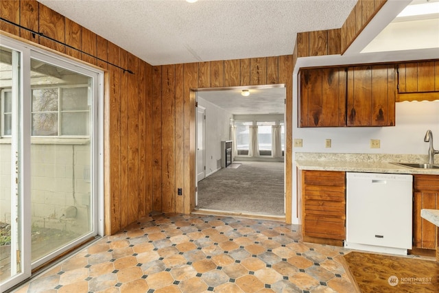 kitchen featuring dishwasher, a textured ceiling, wooden walls, and sink