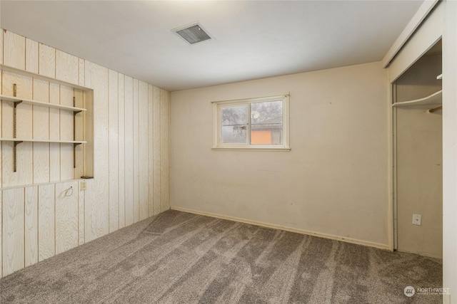 carpeted spare room featuring wooden walls