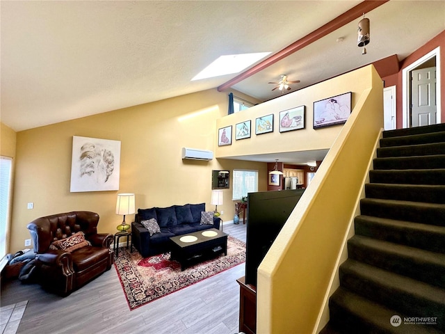 living room with ceiling fan, wood-type flooring, lofted ceiling with skylight, and an AC wall unit