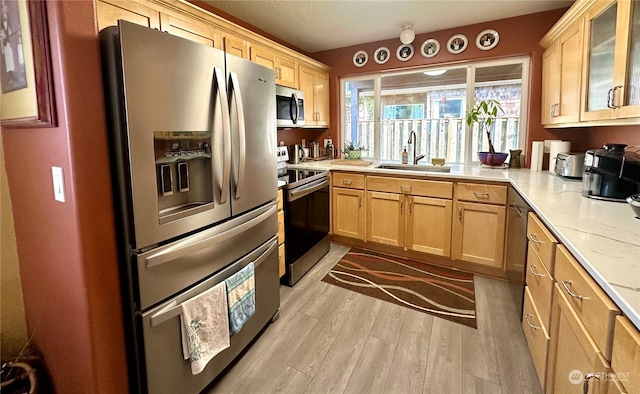 kitchen with light stone countertops, sink, light brown cabinets, stainless steel appliances, and light wood-type flooring