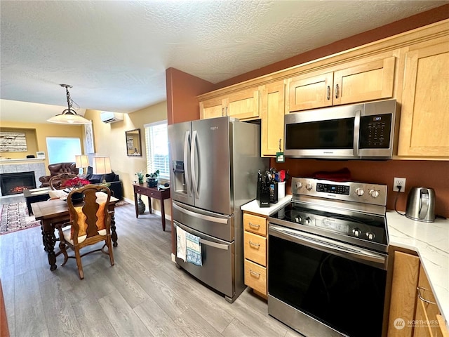 kitchen with a tile fireplace, stainless steel appliances, a wall unit AC, pendant lighting, and light hardwood / wood-style floors