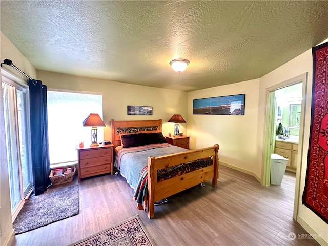 bedroom with wood-type flooring, a textured ceiling, and ensuite bath