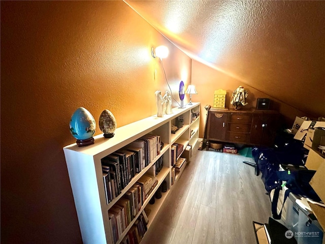 additional living space with a textured ceiling, hardwood / wood-style flooring, and lofted ceiling