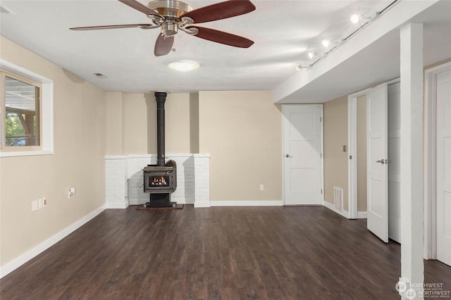 unfurnished living room featuring dark wood-type flooring, a wood stove, and track lighting