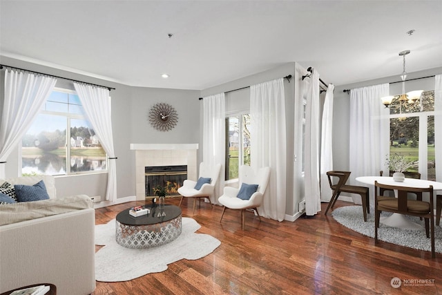 living room with a tiled fireplace, a wealth of natural light, dark hardwood / wood-style flooring, and an inviting chandelier