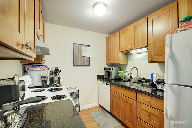 kitchen with dark stone countertops, white appliances, sink, and light hardwood / wood-style flooring