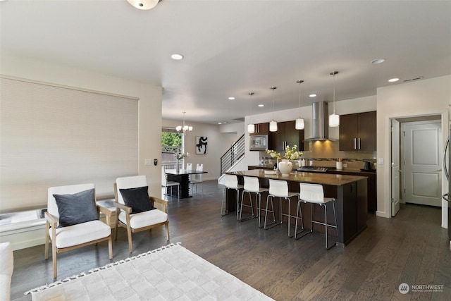 kitchen featuring dark brown cabinets, wall chimney range hood, dark wood-type flooring, and decorative light fixtures