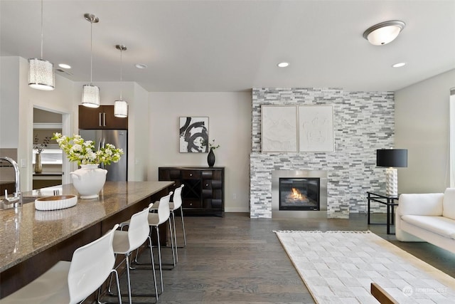 interior space featuring dark wood-type flooring, dark stone counters, decorative light fixtures, a kitchen bar, and stainless steel refrigerator