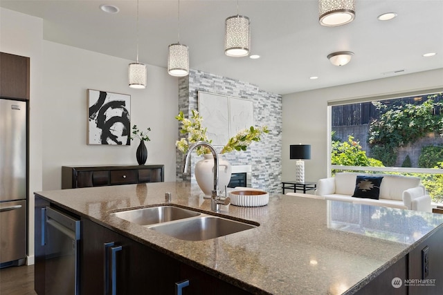 kitchen featuring light stone counters, sink, stainless steel appliances, and hanging light fixtures