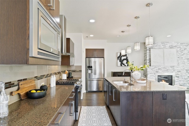 kitchen with sink, hanging light fixtures, a kitchen island with sink, dark brown cabinets, and appliances with stainless steel finishes