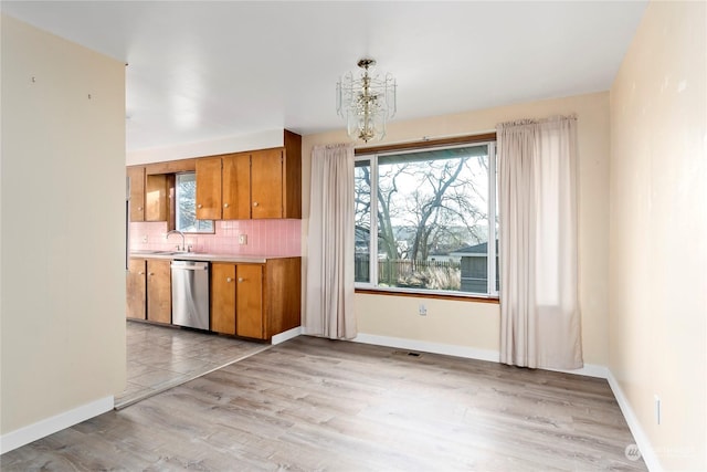 kitchen with backsplash, stainless steel dishwasher, sink, light hardwood / wood-style flooring, and a notable chandelier