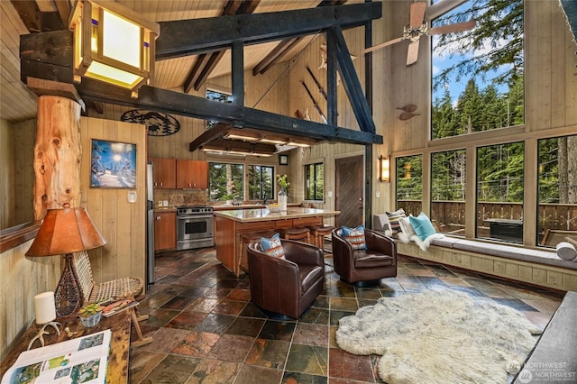 interior space with high vaulted ceiling, ceiling fan, and wood walls