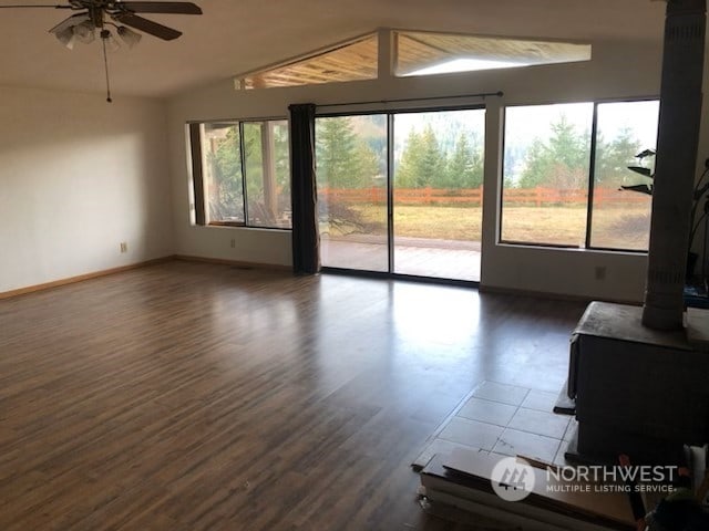 unfurnished living room featuring a wood stove, ceiling fan, dark wood-type flooring, and vaulted ceiling