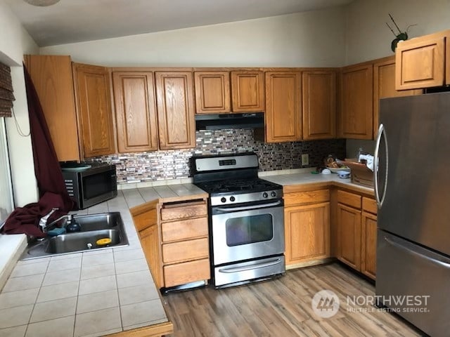 kitchen with sink, range hood, tasteful backsplash, tile counters, and stainless steel appliances