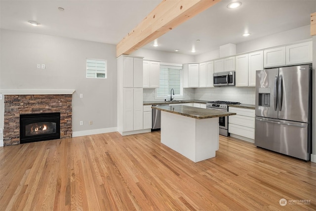 kitchen featuring appliances with stainless steel finishes, a center island, beam ceiling, white cabinets, and backsplash