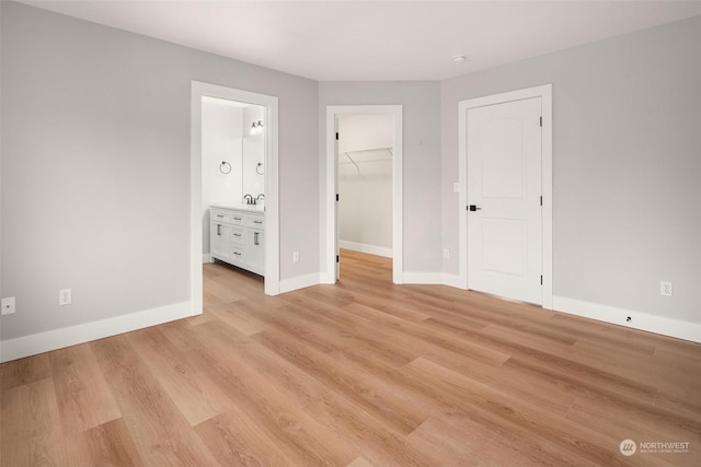 unfurnished bedroom featuring sink, a walk in closet, light hardwood / wood-style flooring, and connected bathroom