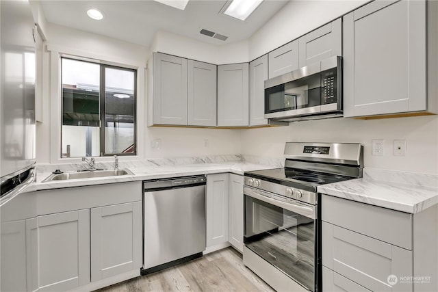 kitchen featuring gray cabinetry, light stone countertops, sink, stainless steel appliances, and light hardwood / wood-style floors