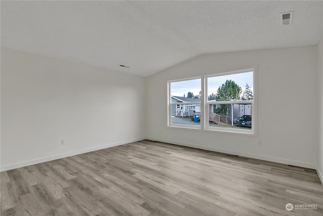 empty room featuring a textured ceiling, light hardwood / wood-style flooring, and vaulted ceiling