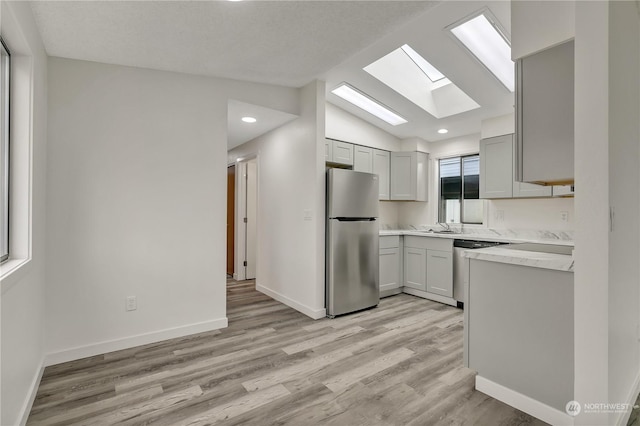 kitchen featuring light wood-type flooring, stainless steel appliances, lofted ceiling with skylight, and gray cabinetry