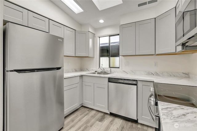 kitchen featuring a skylight, sink, light stone counters, appliances with stainless steel finishes, and light wood-type flooring