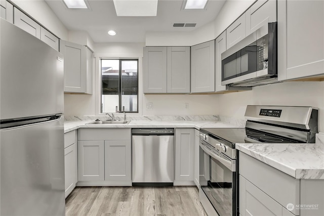 kitchen with appliances with stainless steel finishes, light wood-type flooring, light stone counters, and sink