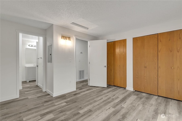 unfurnished bedroom with ensuite bathroom, light hardwood / wood-style floors, a textured ceiling, and multiple closets