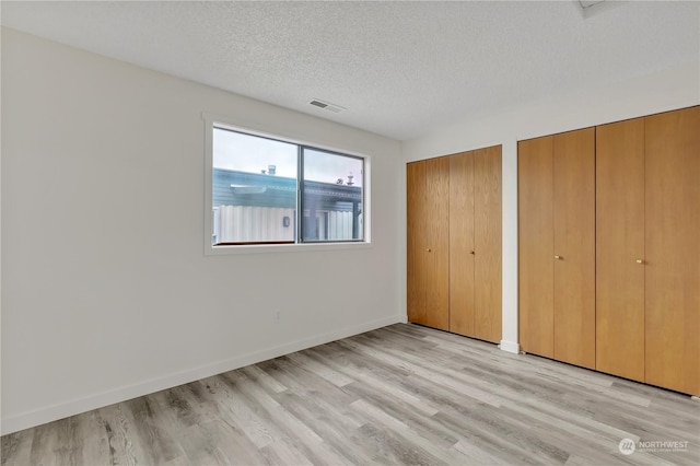 unfurnished bedroom featuring a textured ceiling, two closets, and light wood-type flooring