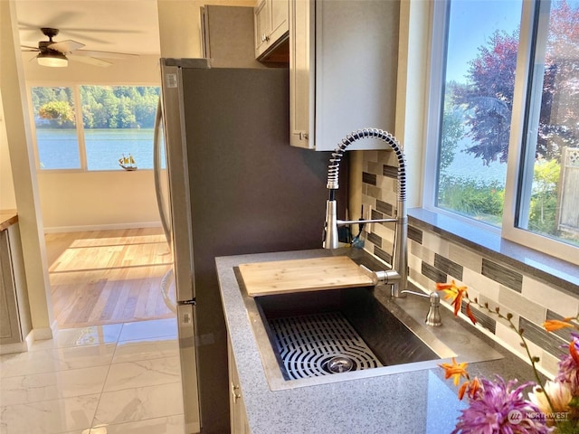 kitchen featuring ceiling fan, sink, backsplash, and a water view