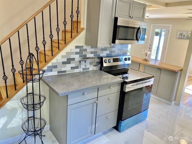 kitchen with gray cabinets, light stone countertops, stainless steel appliances, and tasteful backsplash