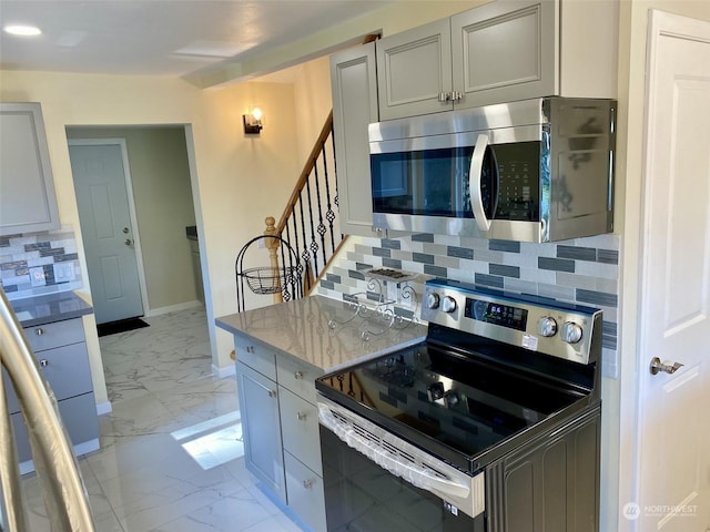 kitchen with decorative backsplash, stainless steel appliances, light stone countertops, and gray cabinetry