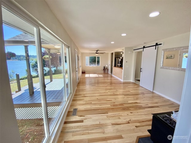 hall featuring a barn door, a water view, a healthy amount of sunlight, and light hardwood / wood-style flooring