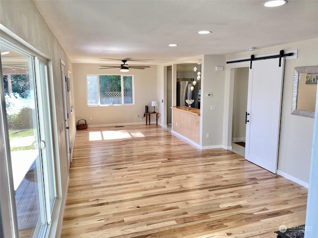 unfurnished room with a barn door, light hardwood / wood-style floors, and ceiling fan