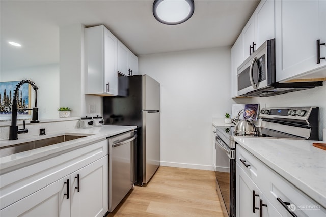 kitchen with light stone countertops, sink, light hardwood / wood-style flooring, white cabinets, and appliances with stainless steel finishes