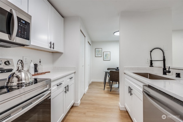 kitchen featuring white cabinetry, sink, light stone counters, appliances with stainless steel finishes, and light wood-type flooring