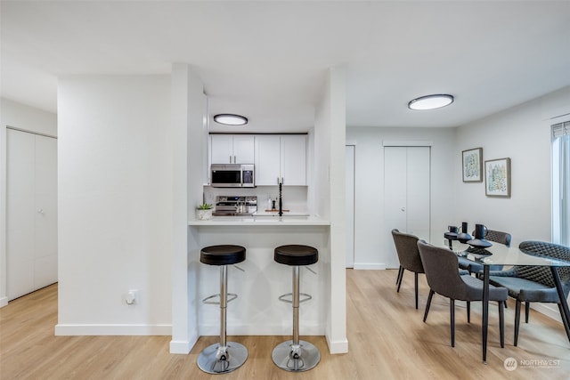 kitchen with stainless steel appliances, kitchen peninsula, a breakfast bar, white cabinets, and light wood-type flooring