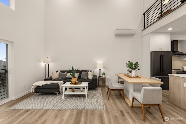 living room with a wall mounted AC, a wealth of natural light, light hardwood / wood-style floors, and a high ceiling