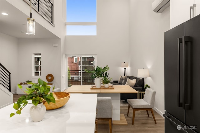 dining room featuring a towering ceiling, a wall mounted air conditioner, and hardwood / wood-style flooring