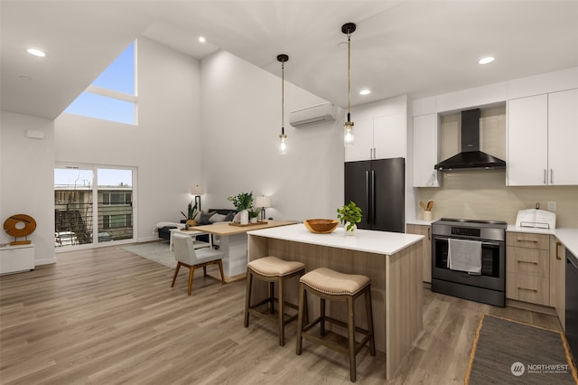 kitchen with stainless steel appliances, a kitchen island, wall chimney range hood, white cabinetry, and hanging light fixtures