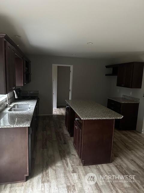 kitchen featuring dark brown cabinetry, sink, a center island, light stone counters, and wood-type flooring