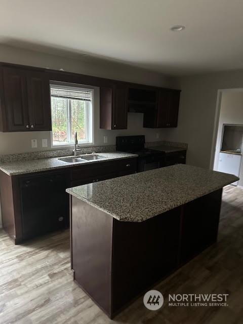 kitchen with dark brown cabinetry, electric range, sink, light stone counters, and a kitchen island