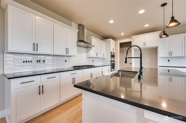 kitchen featuring wall chimney exhaust hood, white cabinetry, hanging light fixtures, light wood-type flooring, and stainless steel appliances