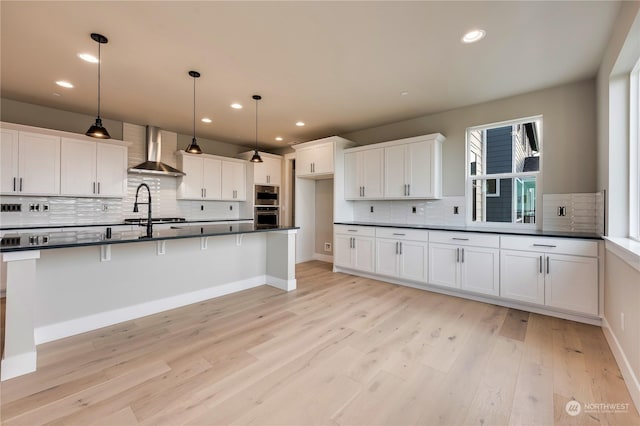 kitchen featuring a breakfast bar area, white cabinetry, light hardwood / wood-style flooring, pendant lighting, and wall chimney range hood